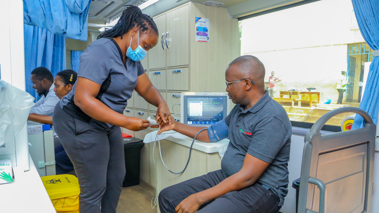 Sarafina Omagwa, a nurse, monitors Safaricom and M-PESA Foundation Senior Programmes Manager Henry Kilonzo’s blood pressure in their mobile clinic during a medical Camp held at Olympic Primary School in Kibera. PHOTO/COURTESY